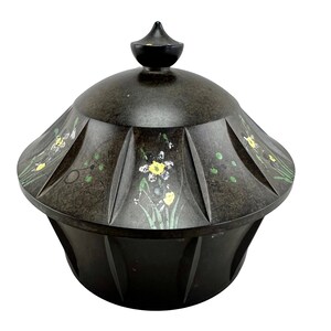 May include: A black ceramic lidded container with a floral design. The container has a rounded base and a domed lid with a pointed top. The floral design features yellow flowers, green leaves, and white accents.