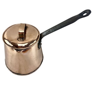 May include: A copper saucepan with a lid and a black iron handle. The saucepan has a hammered finish and a spout.