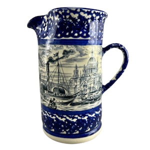Può includere: Brocca in ceramica blu e bianca con una scena di una nave e un edificio sul lato. La brocca ha una glassa blu macchiata.