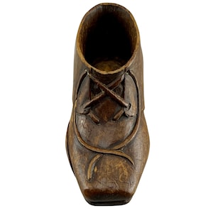 May include: A detailed, carved wooden shoe, seen from above. The shoe is a rich brown hue, featuring visible lacing and a square toe. The interior is hollow, potentially for decorative purposes or as a small container. The craftsmanship is evident.