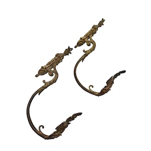 Op de afbeelding: Een paar sierlijke goudkleurige metalen gordijnbandjes met een decoratief rolontwerp.