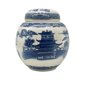 May include: A white ceramic jar with a blue and white floral design. The jar has a lid and is decorated with a traditional Chinese landscape scene.