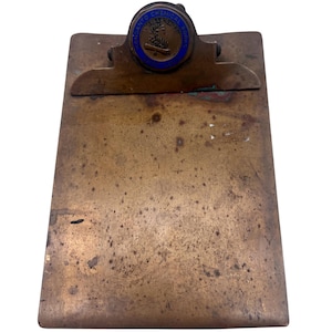 Könnte beinhalten: Ein Vintage-Klemmbrett aus Messing mit einem blauen und goldenen runden Emblem, auf dem "The Ontario Chemical Sales Co." steht.