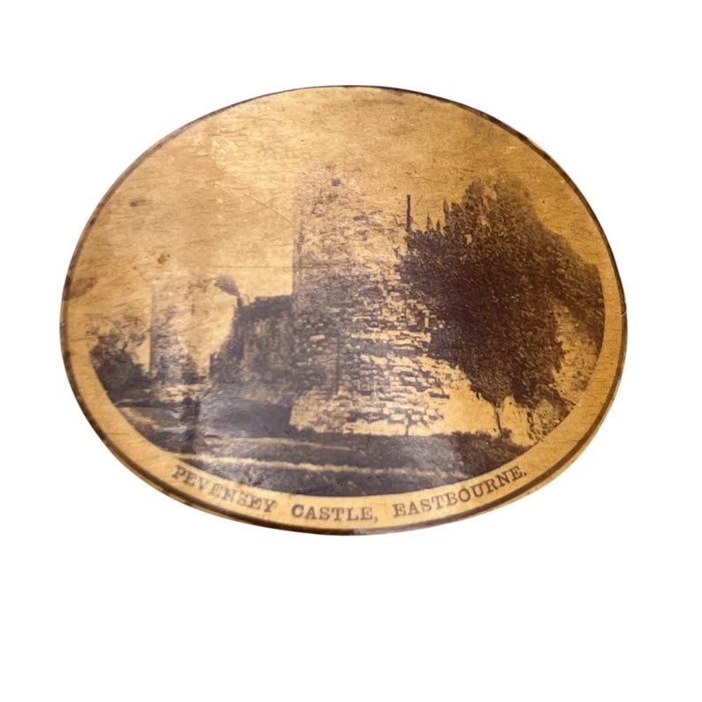 May include: A round wooden coaster with a brown and white image of Pevensey Castle, Eastbourne.