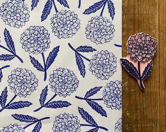 Könnte beinhalten: Ein weißer Hintergrund mit einem sich wiederholenden Muster aus blauen floralen Designs. Die floralen Designs sind stilisiert und ähneln einer Dahlienblüte. Das Bild enthält auch ein separates blaues florales Design mit einem rosafarbenen Zentrum.