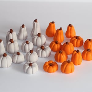 May include: A collection of miniature pumpkins in various shapes and sizes. Some are white, others are bright orange, each with a small brown stem. The pumpkins are arranged on a white surface, perfect for fall decor.