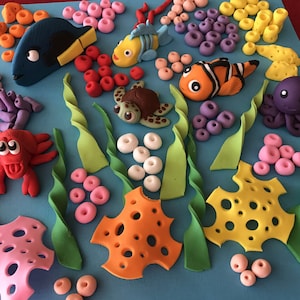May include: A colorful set of fondant cake decorations featuring an underwater scene with a blue fish, a yellow fish, a red crab, a green turtle, an orange starfish, a purple octopus, and coral.