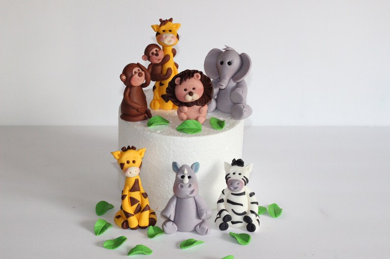 May include: A set of seven fondant animal cake toppers, including a giraffe, monkey, lion, elephant, rhino, zebra, and leaves. The toppers are perfect for a jungle-themed birthday cake.