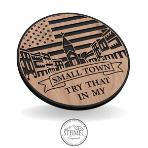 Könnte beinhalten: Ein rundes Holzschild mit einer schwarzen Silhouette einer kleinen Stadt mit einer Kirche und einer amerikanischen Flagge. Das Schild lautet "SMALL TOWN TRY THAT IN MY".