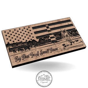 Könnte beinhalten: Ein Holzausschnitt einer amerikanischen Flagge mit einem Leuchtturm, einem Boot und Bäumen im Hintergrund. Der Text "Try That In A Small Town" ist unter dem Bild geschrieben.
