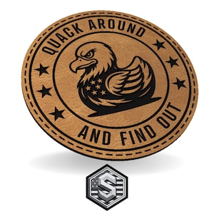 May include: A round, tan leather patch with the text "QUACK AROUND AND FIND OUT" encircling a black graphic of a duck with an eagle's head. The duck has a star-filled chest. A small, silver and white logo is at the bottom.