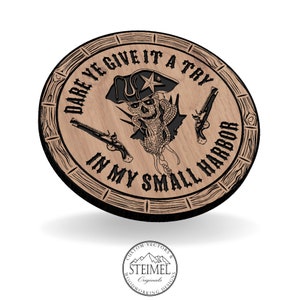 Könnte beinhalten: Ein rundes Holzschild mit einem schwarzen Totenkopf- und Knochen-Piratenmotiv. Das Schild trägt die Aufschrift "Dare ye give it a try in my small harbor".