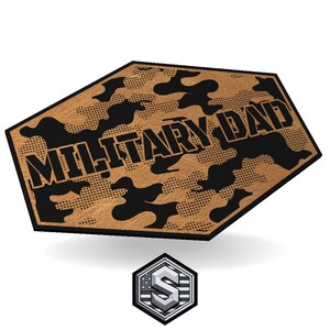 May include: A tan and black camouflage design with the words "MILITARY DAD" in bold black letters. The design is on a hexagonal shape. A smaller, silver and white logo is at the bottom.