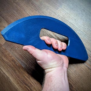 May include: A blue plastic hand grip with a large, curved handle. The grip is designed to help strengthen hand and forearm muscles.