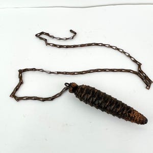 May include: A brown wooden pine cone shaped pendulum with a metal chain.