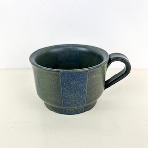 May include: A ceramic mug with a dark green and blue striped design. The mug has a rounded body, a black handle, and a capacity of approximately 12 ounces. The mug is suitable for coffee, tea, or other beverages.