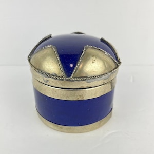 May include: A small, round, blue and silver trinket box with a decorative lid. The lid has a star-shaped design with silver accents.