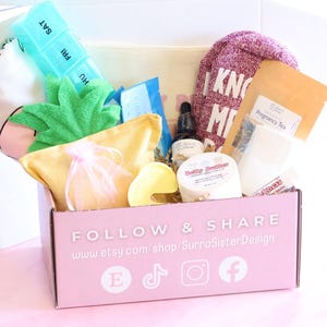 May include: A pink cardboard gift box labelled FOLLOW & SHARE with the URL www.etsy.com/shop/SurraSisterDesign and social media icons. The box contains a turquoise pill organiser, a yellow pouch, a small jar, a tea packet, and fuzzy socks.