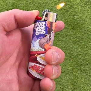 May include: A red and silver lighter with a colorful design featuring a cartoon character and the text "Smoke Good Eat Good".