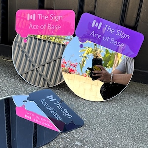 May include: Three circular mirrors, each featuring a speech bubble-shaped acrylic topper in pink, purple, or dark blue. Each topper displays the text "The Sign" and "Ace of Base" in white, along with a small vertical bar icon above the text.