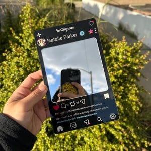 May include: A rectangular black acrylic mirror designed to resemble an Instagram profile interface. It features the text Natalie Parker, a verified checkmark, and social media icons. The center is a reflective surface showing a smartphone reflection.
