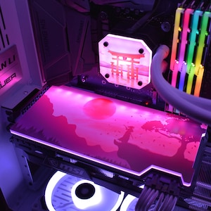 May include: A custom-built computer with a pink and white color scheme. The graphics card features a pink landscape design with a red sun and a silhouette of a figure. The CPU cooler has a Japanese Torii gate design.