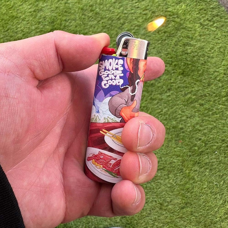 May include: A red and silver lighter with a colorful design featuring a cartoon character and the text "Smoke Good Eat Good".