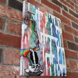 May include: A colorful art print featuring a faucet with water flowing into a teacup. The artwork includes a rainbow, a person, and dripping white paint over a vibrant background of red, blue, and green hues. The print is mounted on a white canvas.