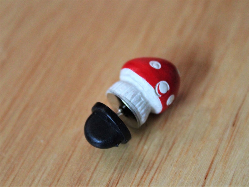 May include: A red and white mushroom shaped pin with a black pin back.