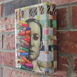May include: A colorful mixed media artwork featuring a woman's face with a cluster of colored pencils covering half of her face. The background is a collage of colorful patterned paper.