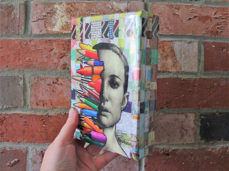 May include: A colorful collage of colored pencils and a woman's face on a small canvas. The canvas is covered in colorful paper scraps and has a glossy finish.