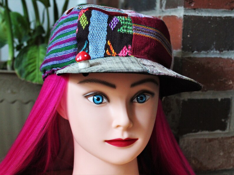 May include: A mannequin head with pink hair wearing a multi-colored patchwork cap with a small red mushroom pin.