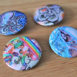 May include: Four round button pins with different colorful designs. One pin features a blue and white octopus, another has a rainbow and unicorn design, another has a blue and white abstract design, and the last one has a black and white abstract design.