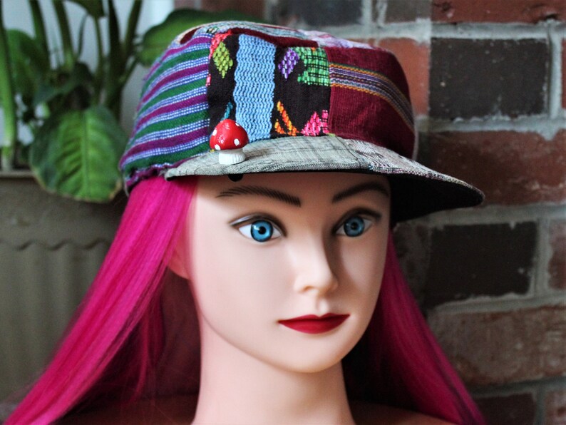 May include: A colorful patchwork fabric cap with a mushroom pin. The cap has a flat brim and is made of a variety of fabrics in different colors and patterns.