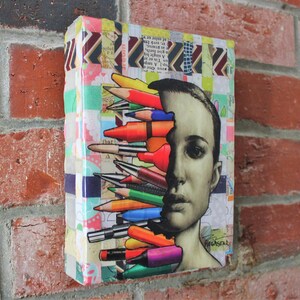 May include: A colorful collage artwork featuring a person's face with a variety of colored pencils and markers sticking out of their head. The background is a patchwork of colorful patterns.