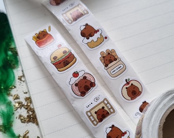 May include: Two rolls of adhesive stickers featuring cartoon capybaras in various food-themed designs, including burgers, fries, apples, and desserts. Some stickers include the text "Love" or "CAPY BARA" in a small, clear font.