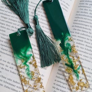 May include: Two rectangular resin bookmarks featuring a deep forest green solid top section that transitions into a clear base filled with swirling green ink patterns and scattered gold leaf flakes, each finished with a matching green silk tassel.