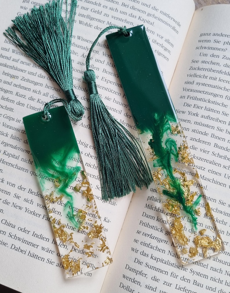 May include: Two rectangular resin bookmarks featuring a deep forest green solid top section that transitions into a clear base filled with swirling green ink patterns and scattered gold leaf flakes, each finished with a matching green silk tassel.