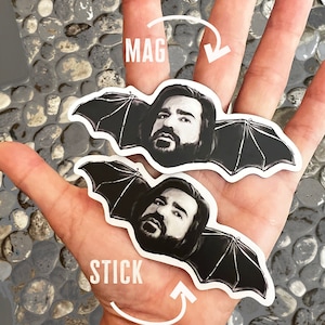 May include: Two black and white stickers of a man with a beard and wings. The stickers are on a hand, one is labeled "MAG" and the other is labeled "STICK".