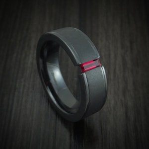 May include: A black tungsten carbide ring with a red gemstone inlay.