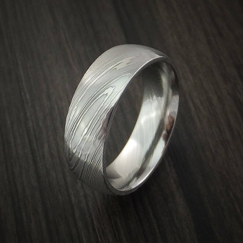 May include: A silver wedding band with a brushed metal finish and a unique patterned design.