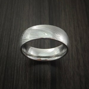 May include: A silver-toned ring with a unique, textured pattern. The ring is made of metal and has a polished finish.