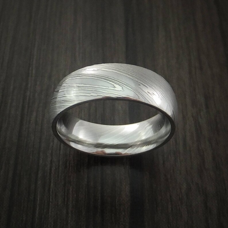 May include: A silver-toned ring with a unique, textured pattern. The ring is made of metal and has a polished finish.