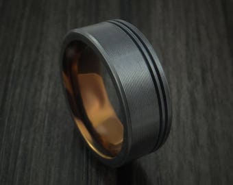 May include: A black ring with a brushed finish and two grooves. The ring has a gold inner band.