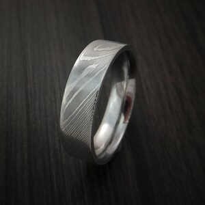May include: A silver wedding band with a unique, patterned design. The band is made of metal and has a polished finish.