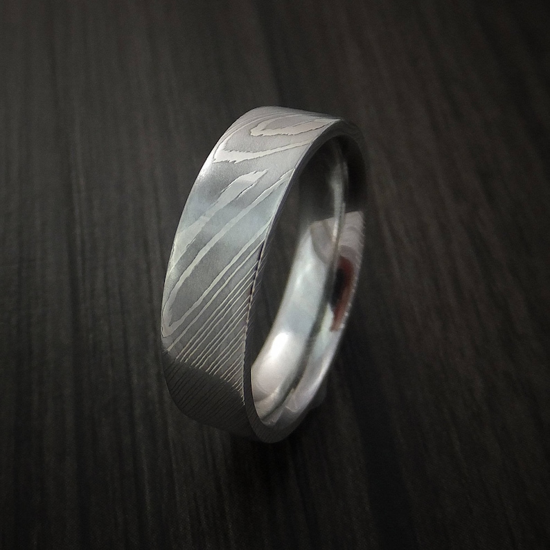 May include: A silver wedding band with a unique, patterned design. The band is made of metal and has a polished finish.