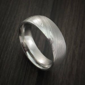 May include: A silver wedding band with a unique, textured pattern. The band is made of metal and has a polished finish.