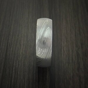 May include: A silver ring with a patterned design. The ring is made of metal and has a smooth finish.