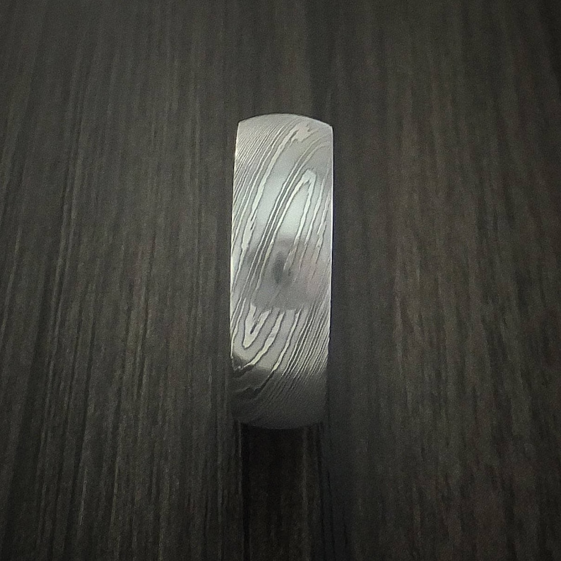 May include: A silver ring with a patterned design. The ring is made of metal and has a smooth finish.