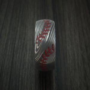 Puede incluir: Un anillo de plata con un dise&ntilde;o de puntadas de b&eacute;isbol. Las puntadas son rojas y el anillo tiene un acabado de metal cepillado.